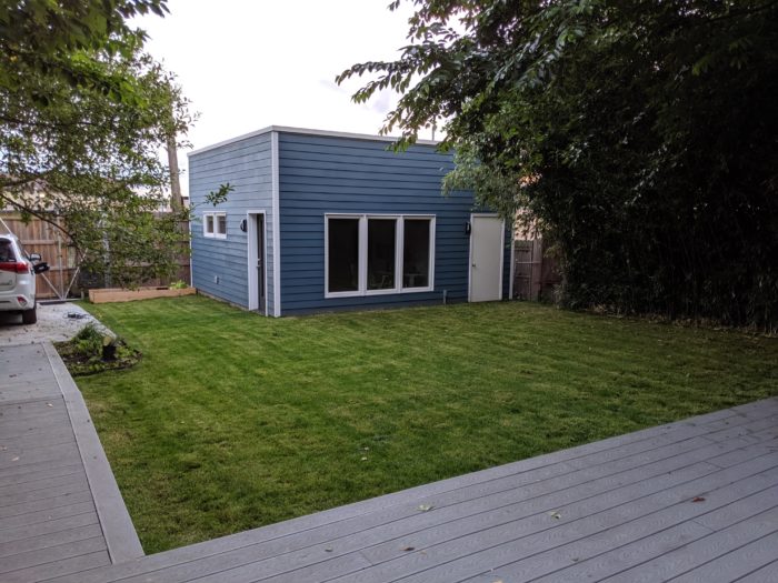 Blue square office in a back yard with a grass yard around it.
