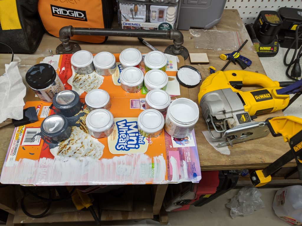 A number of cut aluminum cans turned upside-down and painted white. A jigsaw sits to the right of the cans.
