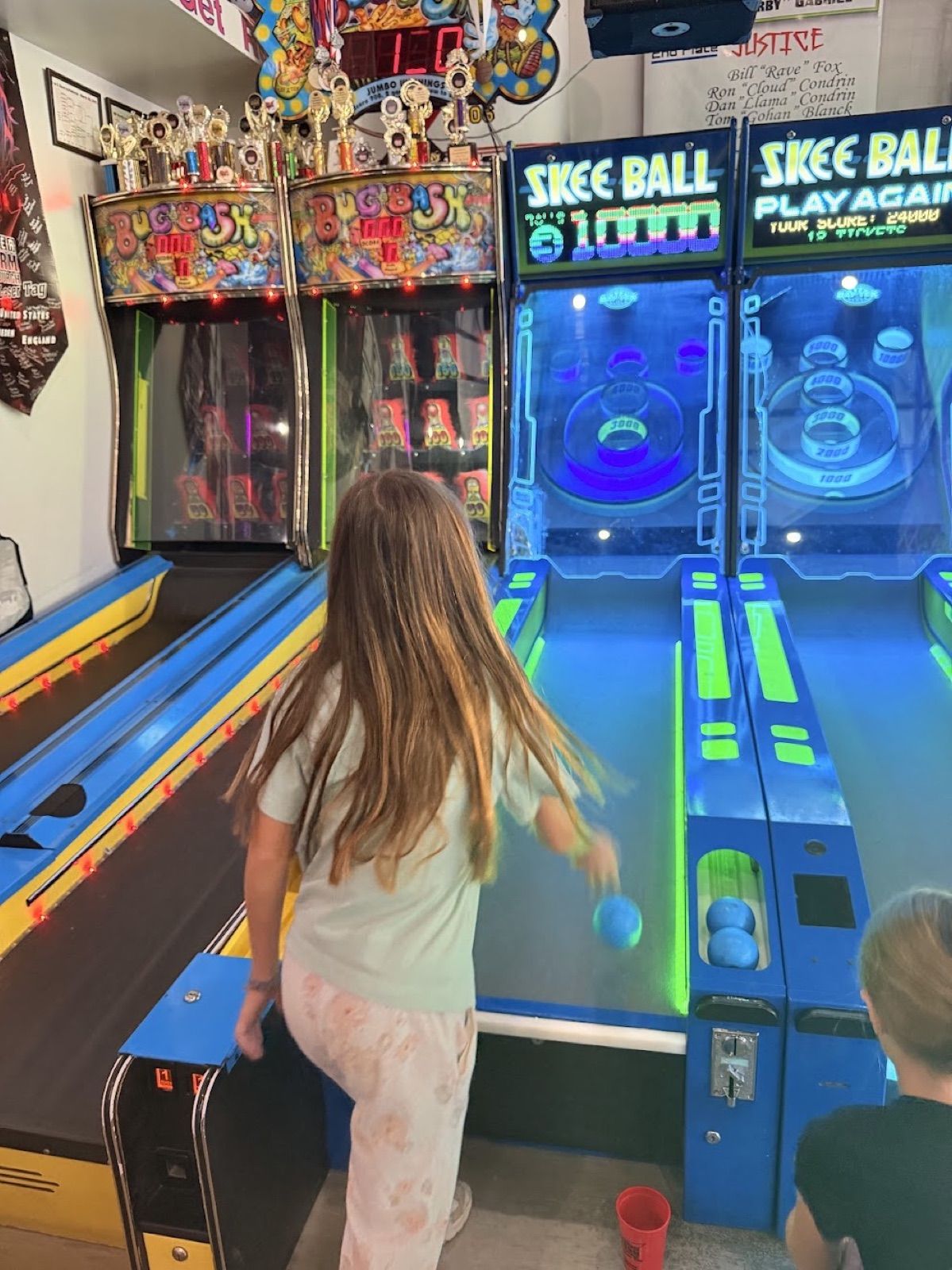 A kid rolling a ball up a glowing Skee-Ball lane