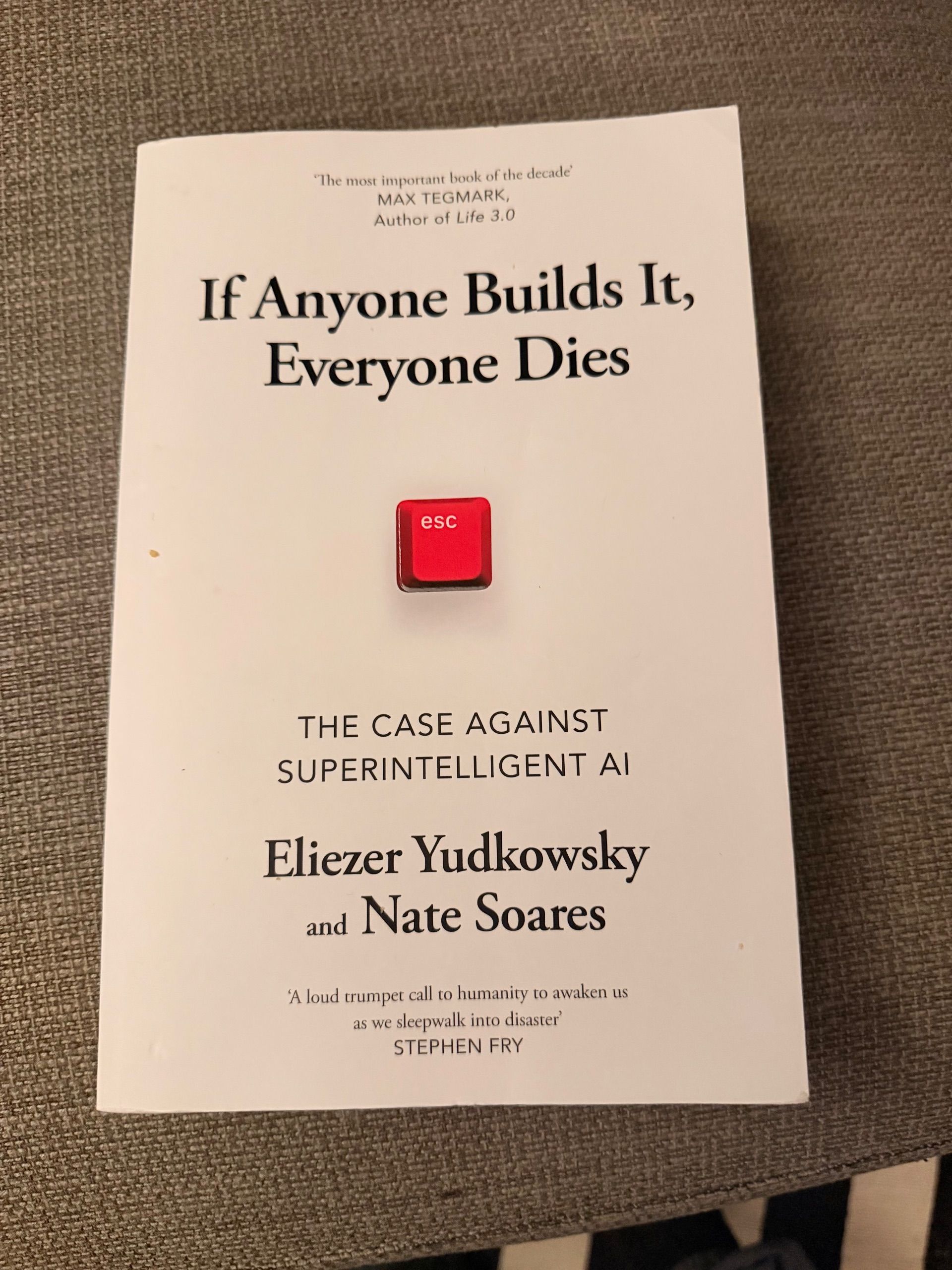 Book cover titled "If Anyone Builds It, Everyone Dies: The Case Against Superintelligent AI" by Eliezer Yudkowsky and Nate Soares, featuring a red escape key button in the center, on a textured fabric surface.