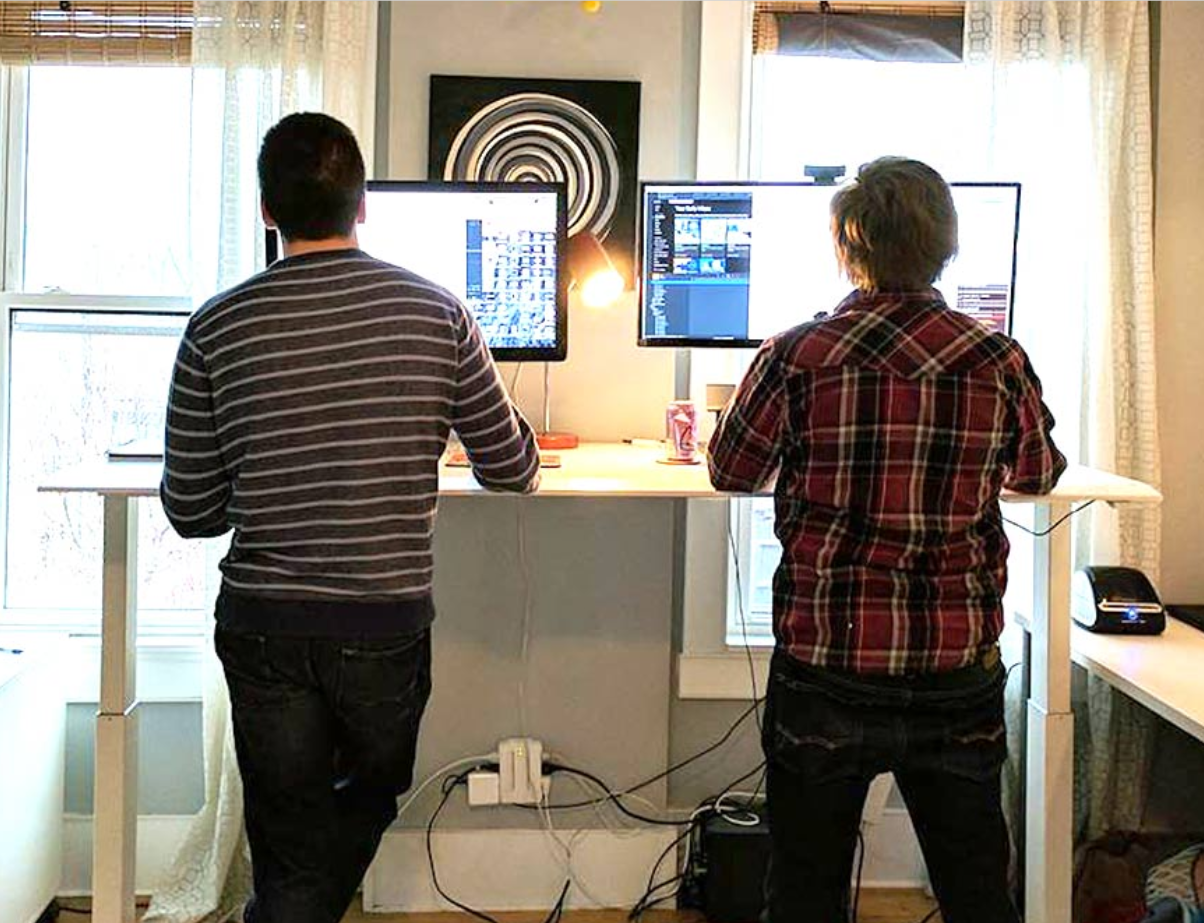 Brad and Ian standing at a shared standing desk looking at their computers