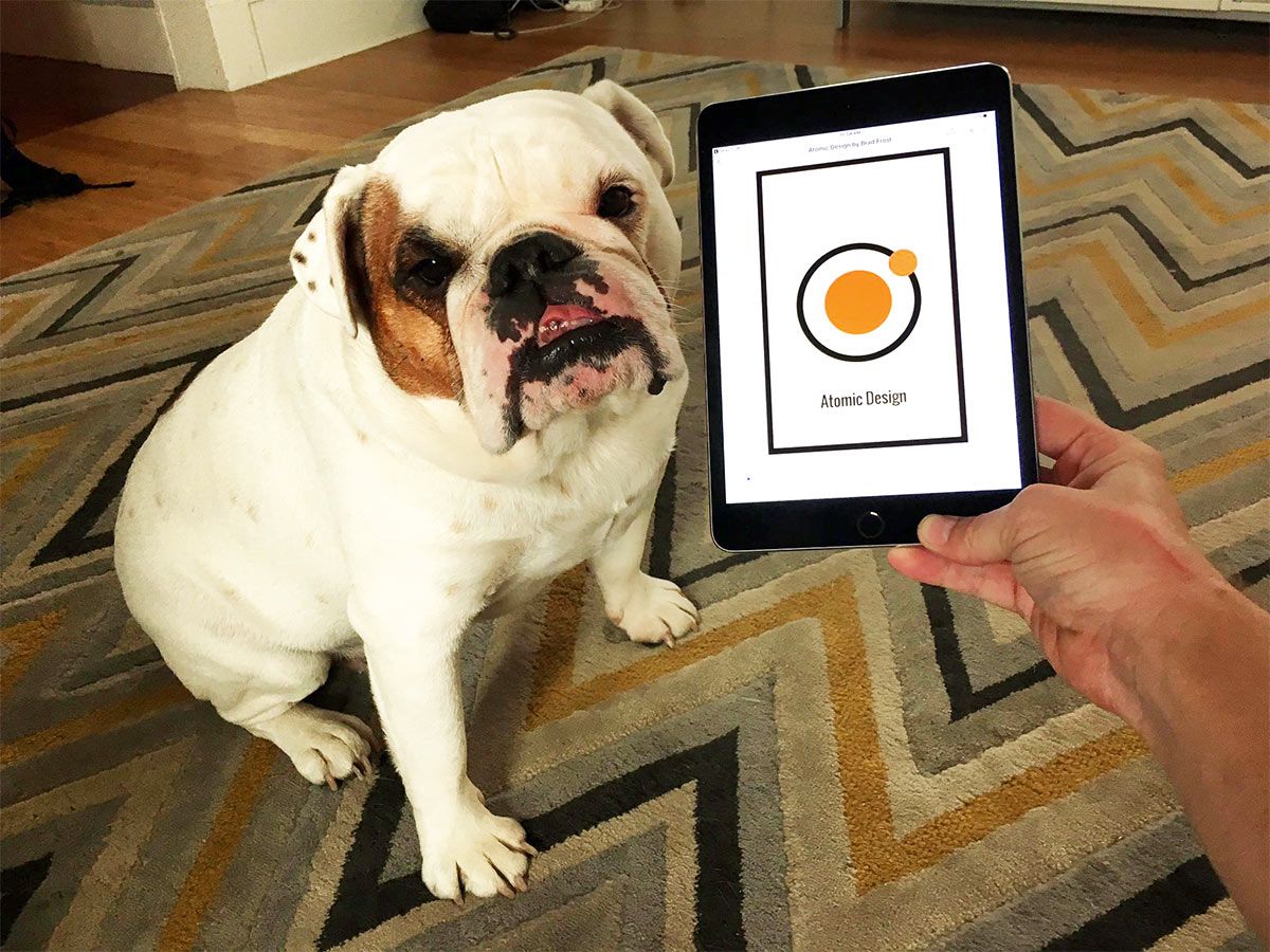 A bulldog sitting beside a tablet showing the Atomic Design ebook