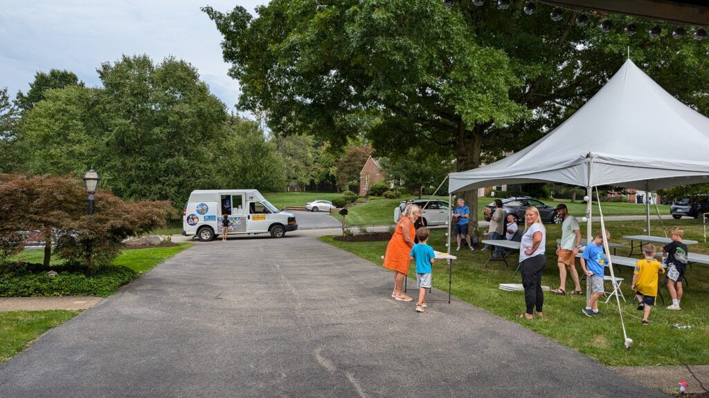 An ice cream truck at the end of Brad's driveway. People and a party tent