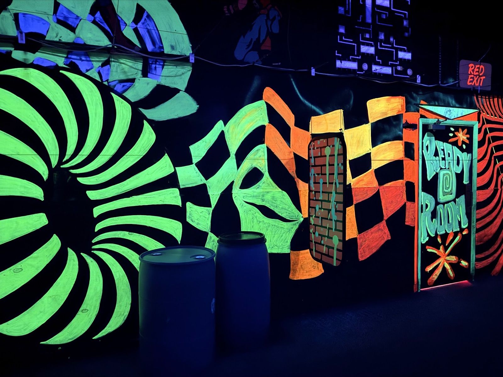 A glowing wall of green and black tunnels, orange checkerboards, and a "Ready Room" door, with blue barrels in front
