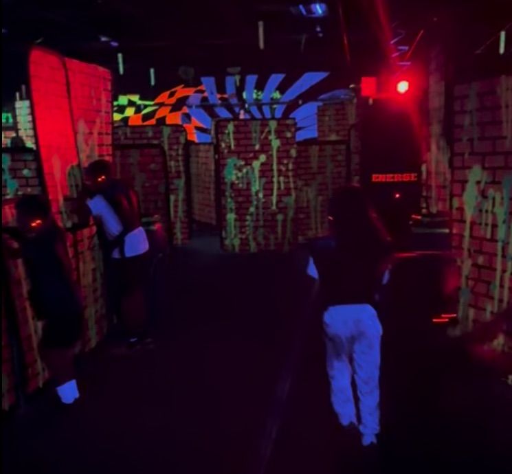 Kids running through the dark, blacklit arena past painted brick barriers
