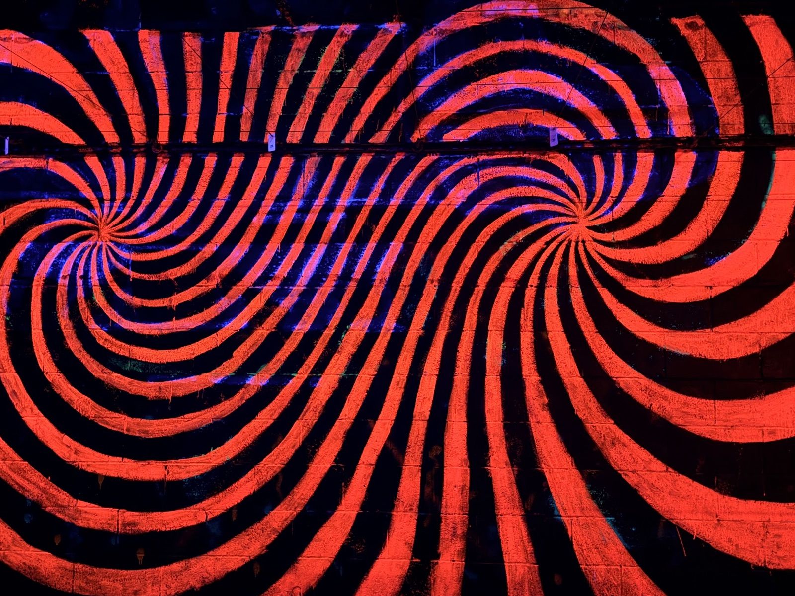 A blacklit wall painted with two red-and-black swirling spirals