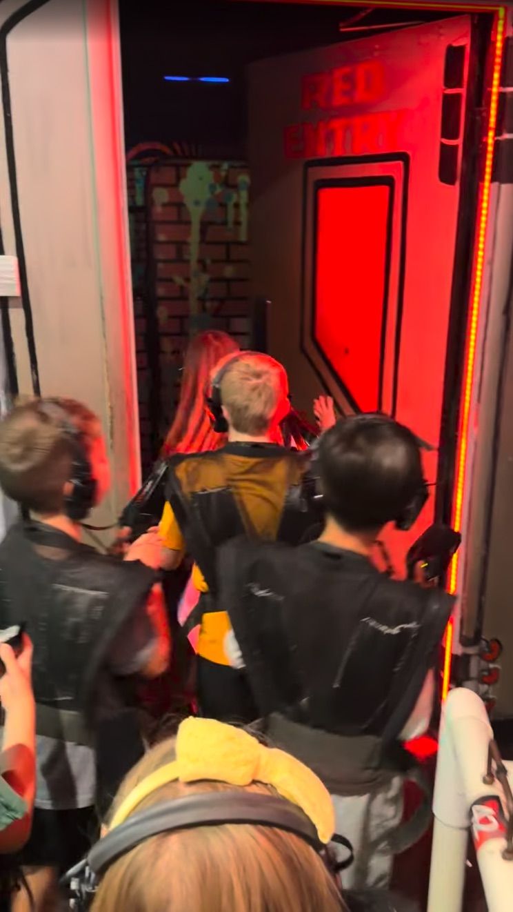 Kids in laser tag vests and headsets lining up at a red-lit door into the arena
