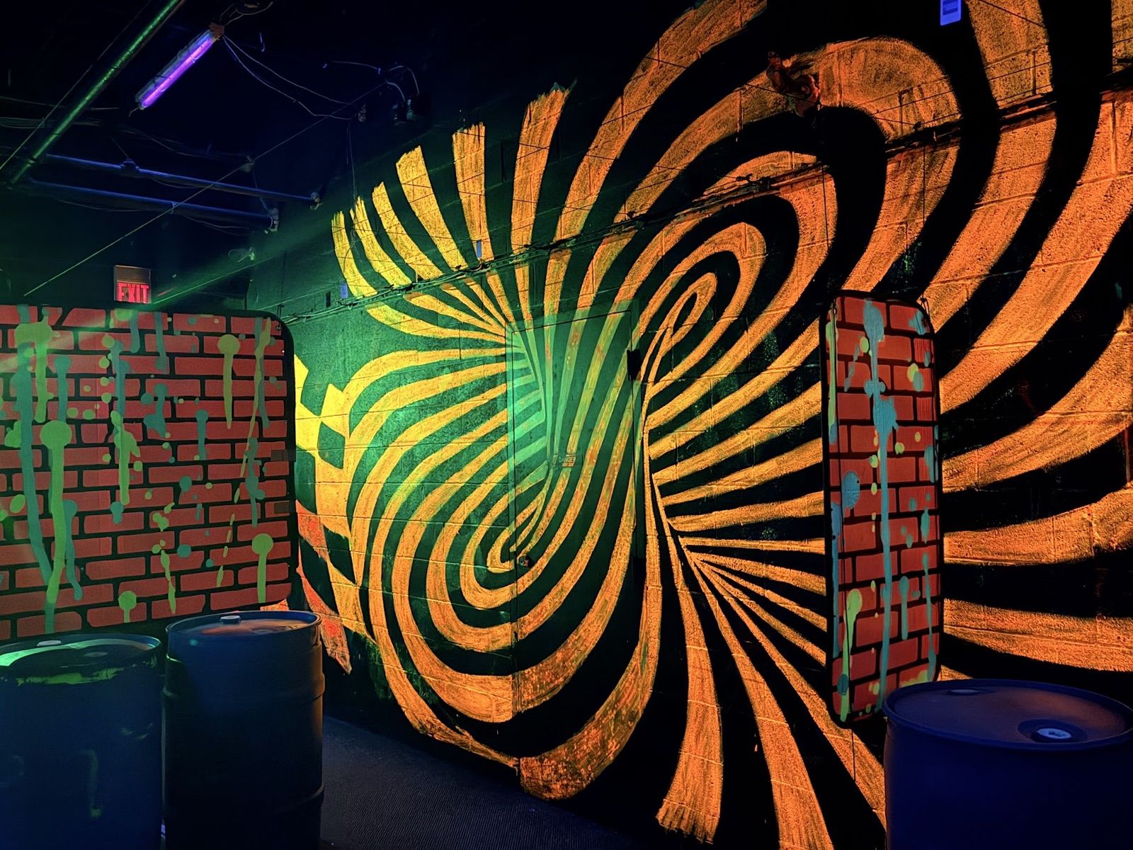 An orange-and-black spiral vortex painted across a wall, flanked by fake brick barriers dripping with green paint