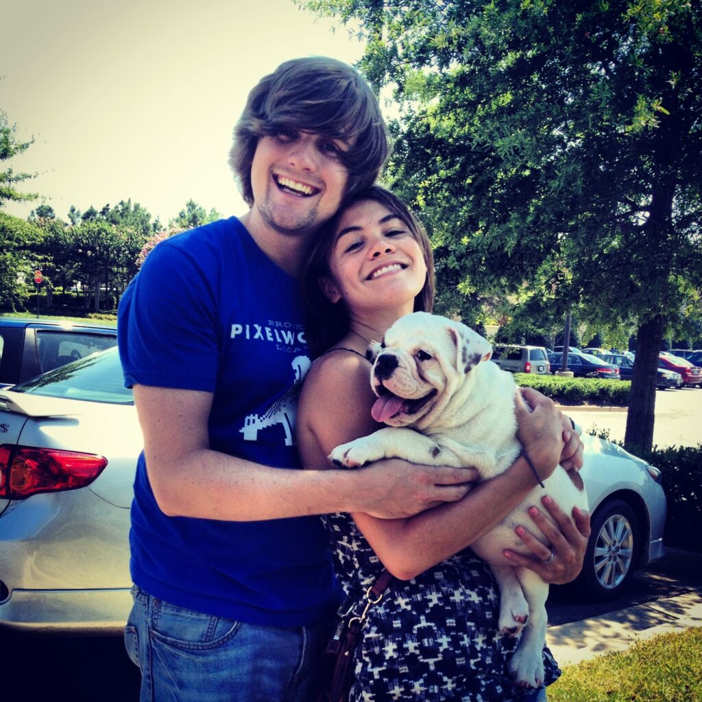 A shaggy-haired Brad and Melissa smiling with Ziggy the puppy in their arms