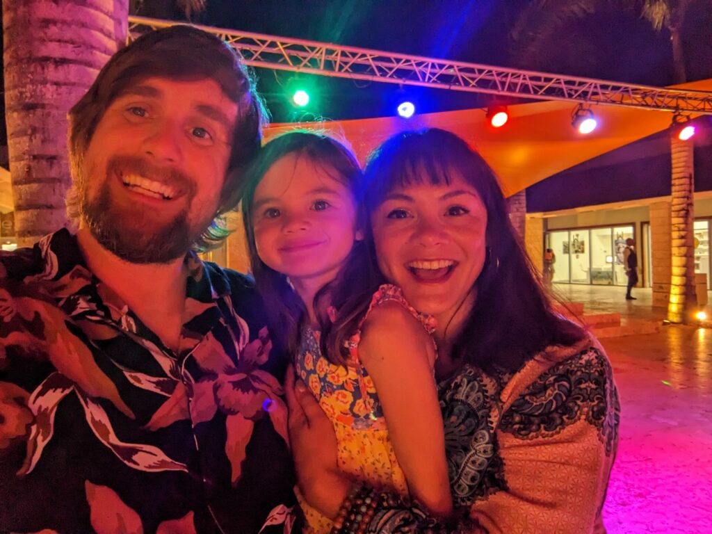 Brad, Melissa, and Ella smiling at the camera under some red stage lights 