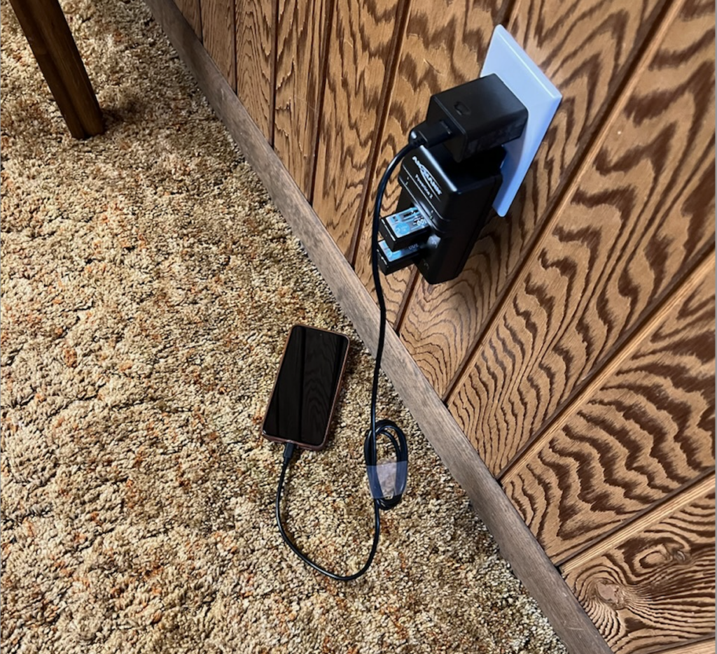 Brad's phone sitting on a brown shag carpet plugged into an outlet.