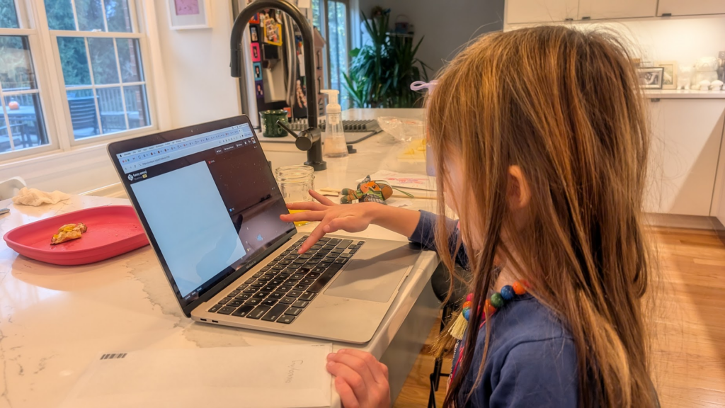 Ella on Brad's laptop sitting at the breakfast table