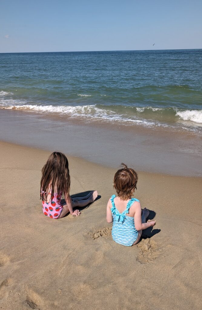 Two little girls sitting in the sand looking out at the Atlantic Ocean