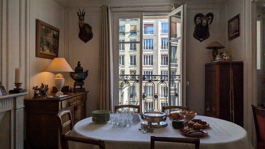 A Parisian dining room with open windows looking out at a French building facade