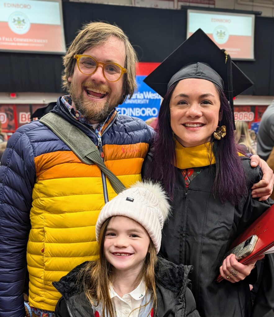 Melissa in her cap and gown smiling with Ella and Brad