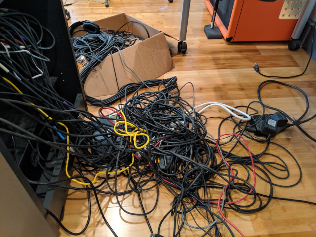 A rats nest of instrument cables and other wires spewing forth onto a wooden floor